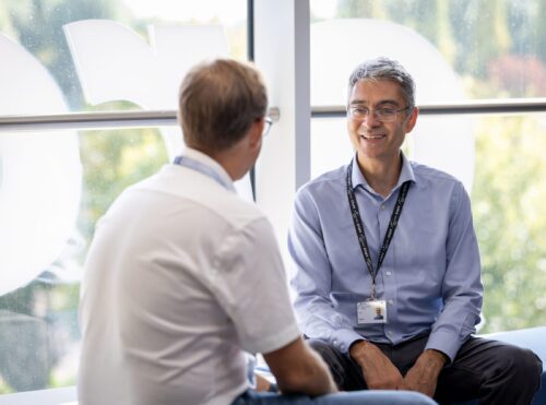 Renos Savva talking to team member in window seat